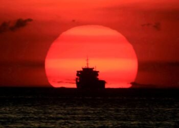 A cargo ship is silhouetted as the sun sets along the coast of Manila bay