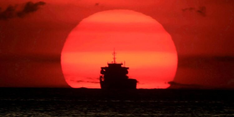 A cargo ship is silhouetted as the sun sets along the coast of Manila bay
